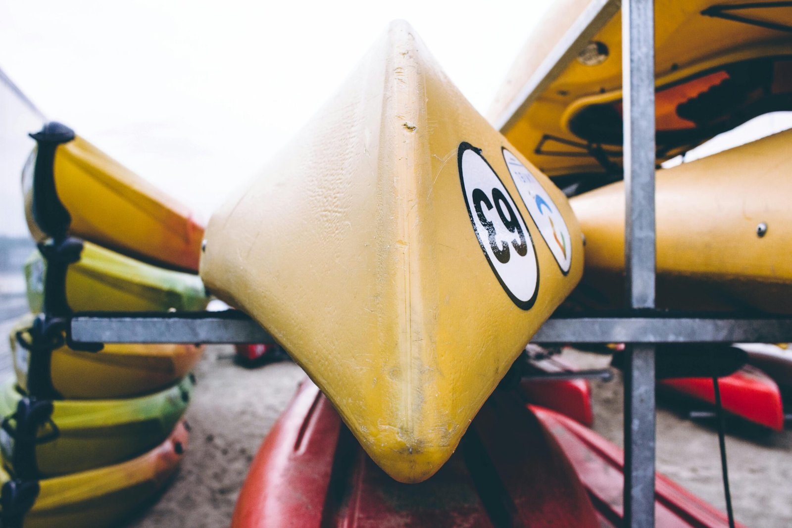 A detailed view of brightly colored kayaks stacked outdoors, focusing on a yellow kayak with numbers.