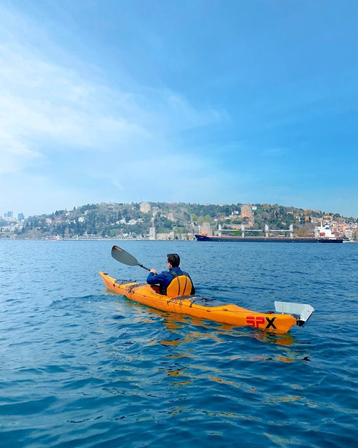 A person kayaking on a sunny day on vibrant blue waters, with lush green hills in the background.